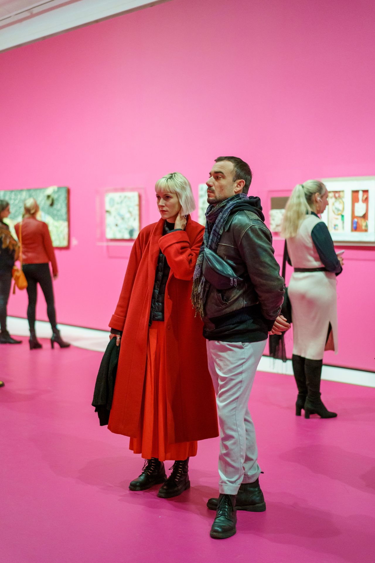 Zwei Personen in einem Kunstausstellungsraum mit pinken Wänden, umgeben von anderen Besuchern.