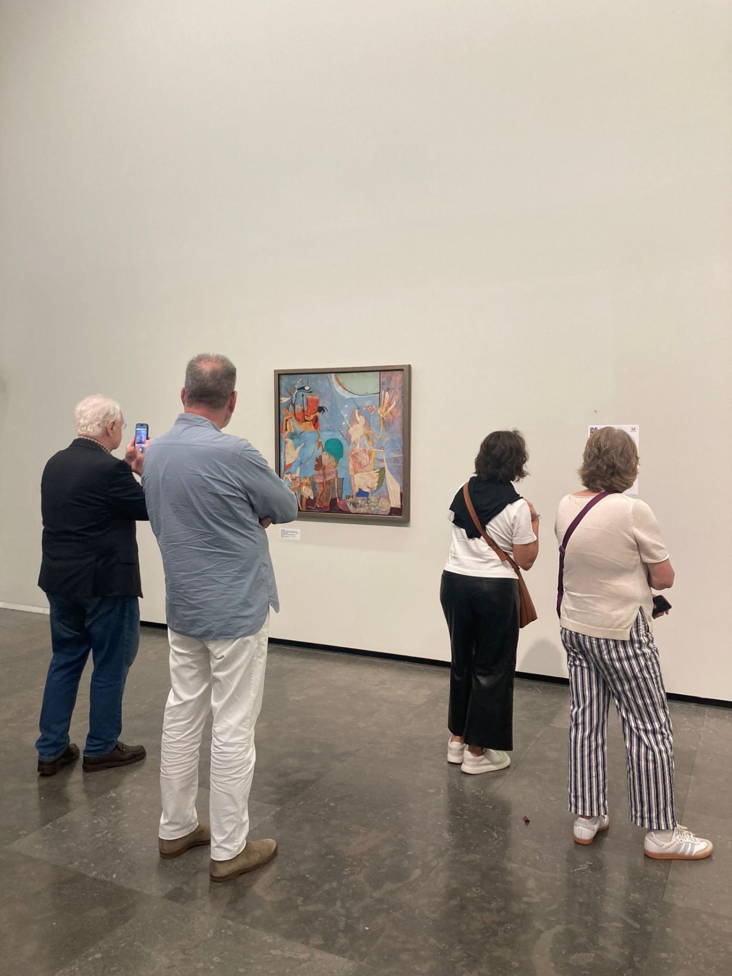 Besucher betrachten ein Gemälde in einem modernen Museum mit heller, minimalistischer Wand im Hintergrund.
